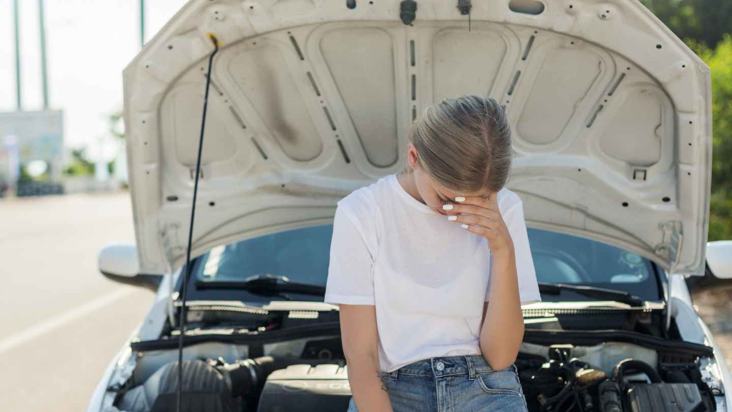 Driver sitting in front of an open hood looking frustrated