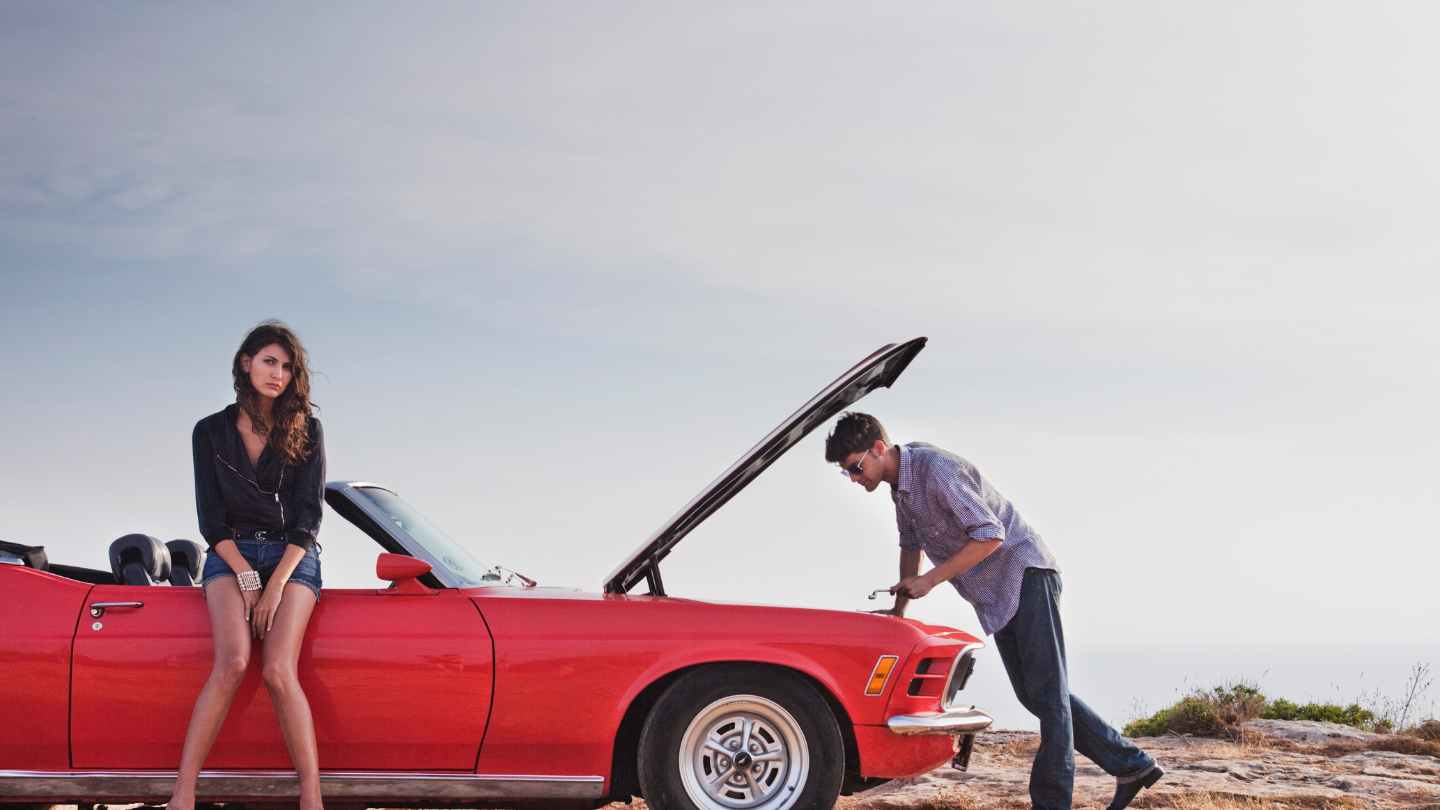 Couple dealing with a broken-down convertible on the roadside