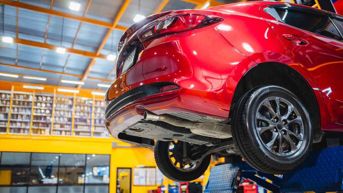 Used red car being inspected on a repair-shop lift