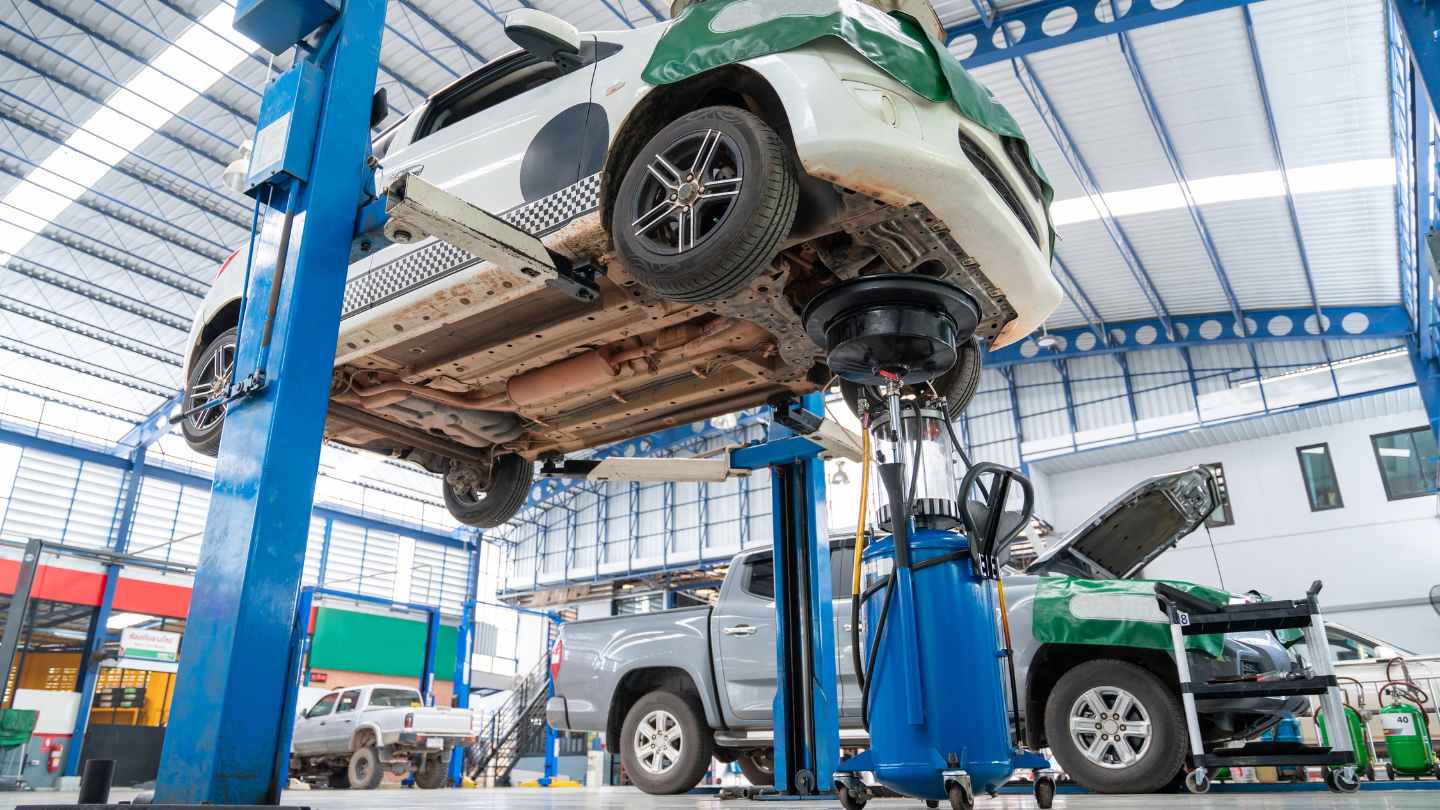 Technician inspecting a white car on a lift to diagnose a repair